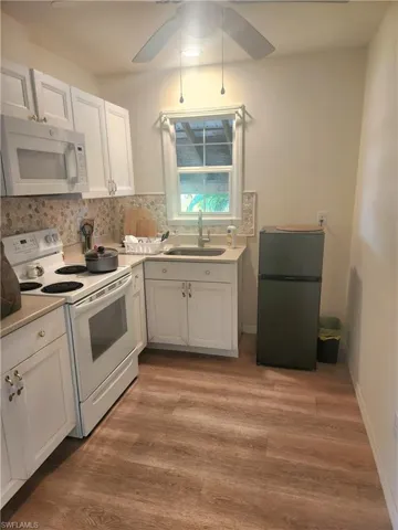 Kitchen featuring white appliances, light wood finished floors, white cabinets, a ceiling fan, and a sink