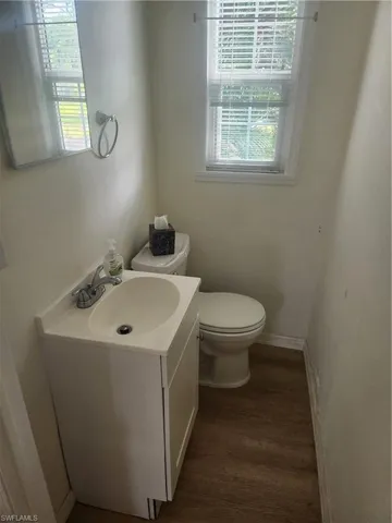 Half bathroom with baseboards, vanity, toilet, and wood finished floors