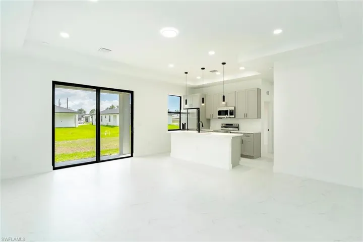 Kitchen with open floor plan, decorative light fixtures, a center island with sink, gray cabinets, and recessed lighting