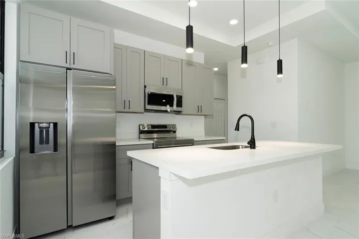 Kitchen with appliances with stainless steel finishes, light marble finish flooring, gray cabinetry, hanging light fixtures, and recessed lighting