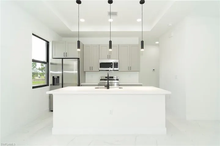 Kitchen with appliances with stainless steel finishes, a tray ceiling, decorative light fixtures, a kitchen island with sink, and gray cabinets