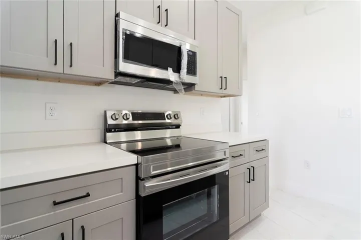 Kitchen with appliances with stainless steel finishes, light countertops, gray cabinets, and light marble finish flooring
