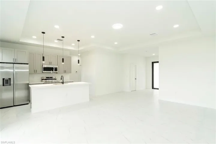 Kitchen with a raised ceiling, appliances with stainless steel finishes, an island with sink, decorative light fixtures, and recessed lighting
