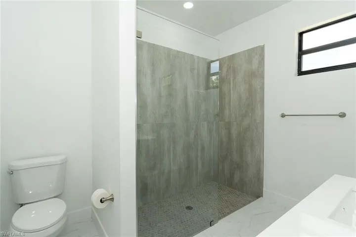 Bathroom featuring plenty of natural light, a stall shower, marble look tiles, and recessed lighting