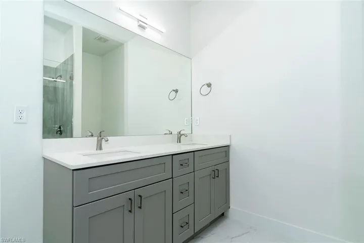 Bathroom with double vanity, light marble finish flooring, and a shower stall