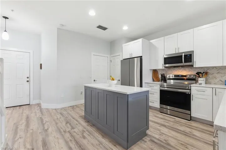 Kitchen featuring decorative light fixtures, stainless steel appliances, white cabinets, and a kitchen island