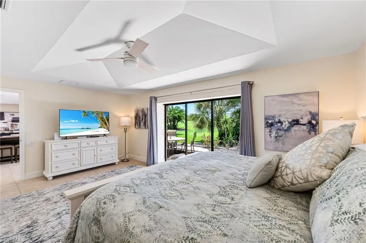 Bedroom featuring a raised ceiling, access to exterior, light tile patterned floors, and ceiling fan