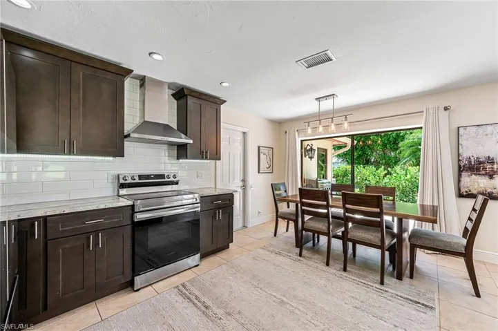 Kitchen with backsplash, electric stove, light stone countertops, wall chimney exhaust hood, and pendant lighting