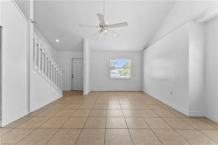 Unfurnished living room with baseboards, vaulted ceiling, light tile patterned floors, a ceiling fan, and stairs