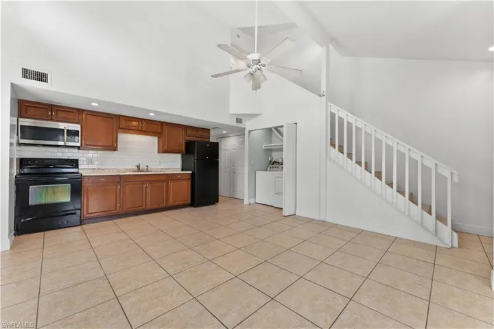 Kitchen with high vaulted ceiling, visible vents, black appliances, washing machine and clothes dryer, and light countertops
