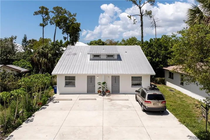 View of front facade with metal roof, stucco siding, fence, and a front lawn
