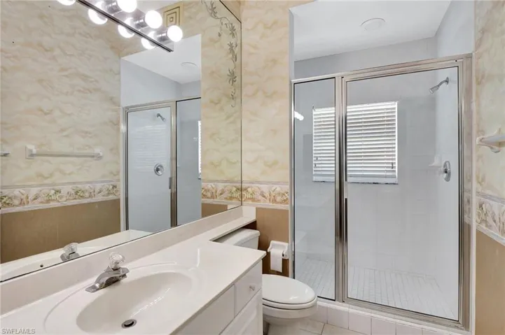 Bathroom with toilet, a stall shower, vanity, and wallpapered walls