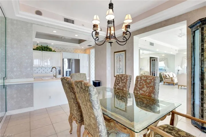 Dining space featuring light tile patterned flooring, visible vents, ornamental molding, wallpapered walls, and a tray ceiling