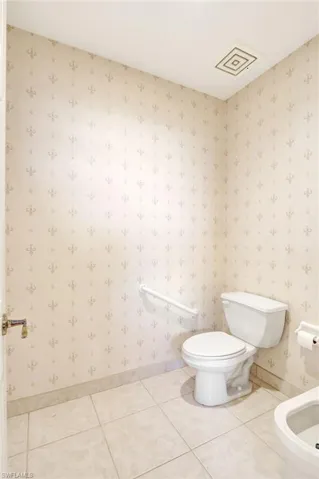 Bathroom with baseboards, wallpapered walls, toilet, and tile patterned flooring