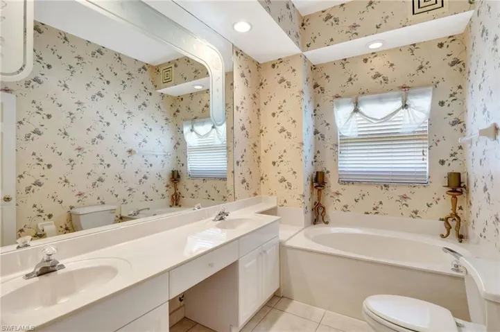 Full bathroom with tile patterned flooring, toilet, wallpapered walls, a sink, and a bath