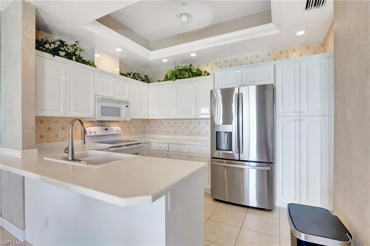 Kitchen featuring a tray ceiling, a peninsula, visible vents, white appliances, and wallpapered walls