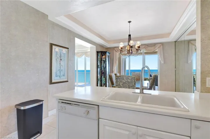Kitchen with white cabinets, a chandelier, dishwasher, a raised ceiling, and a sink