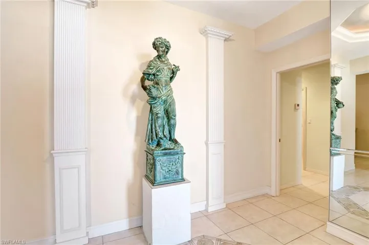Corridor with light tile patterned floors, baseboards, and ornate columns