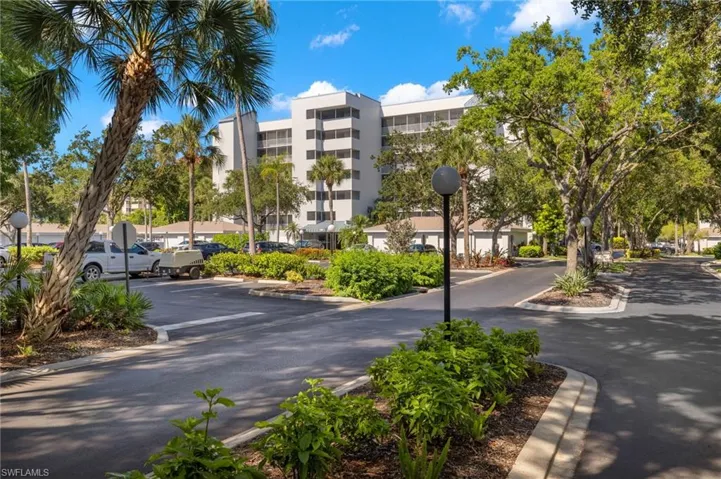 Expansive community grounds featuring a multi-story building, mature trees, manicured landscaping, paved roadways, and dedicated parking areas