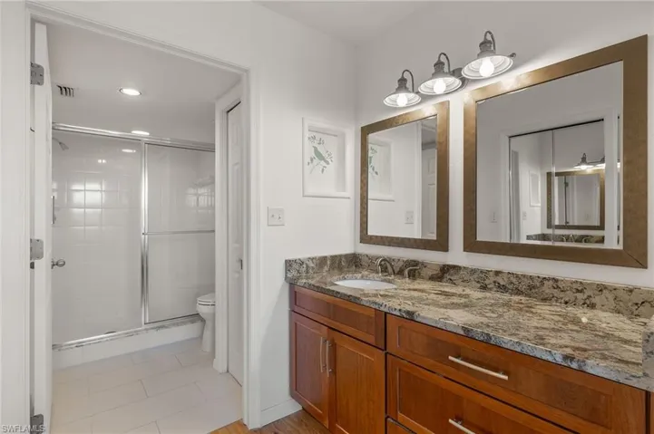 Bathroom featuring a double vanity with stone countertops, individual framed mirrors, and a three-light fixture