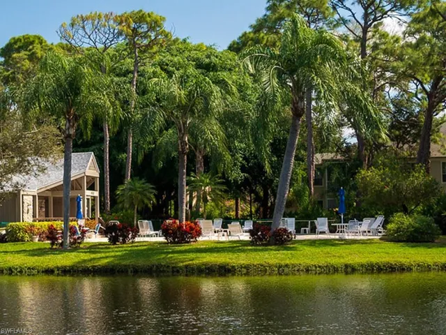 Waterside amenity area featuring a clubhouse with a gabled roof, lush tropical landscaping, and a paved patio