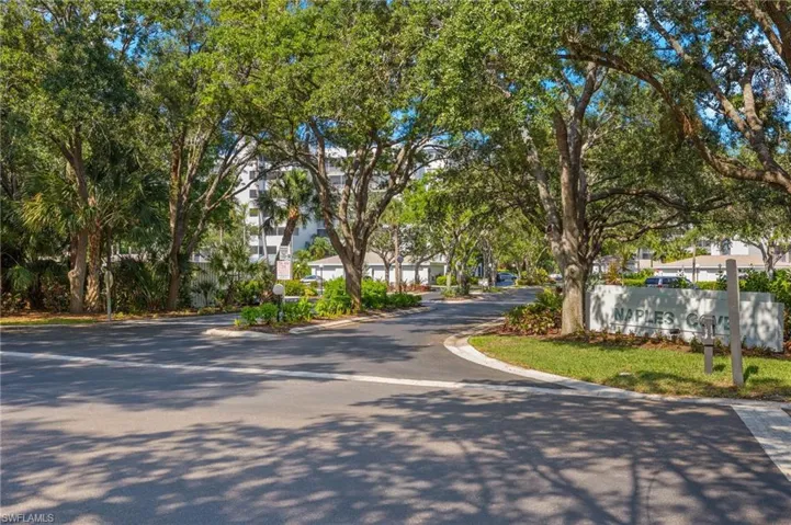 Paved community entrance featuring mature trees, landscaped islands, and a prominent "NAPLES COVE" monument sign