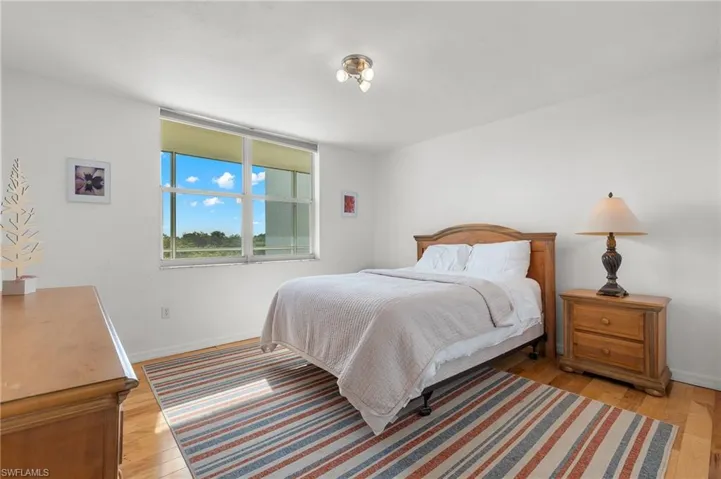 Bright interior space featuring a large window with roller shades, wood-finish flooring, and a flush-mount ceiling light fixture