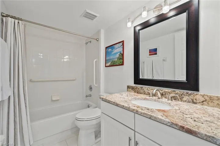 Bathroom featuring a white vanity with a light-colored stone countertop, an undermount sink, and a framed mirror