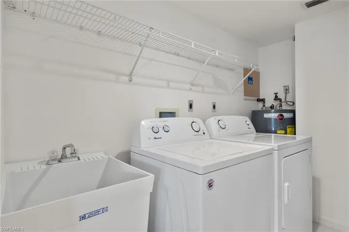 Dedicated laundry space featuring a utility sink with dual-handle faucet, side-by-side washer and dryer, and overhead wire shelving