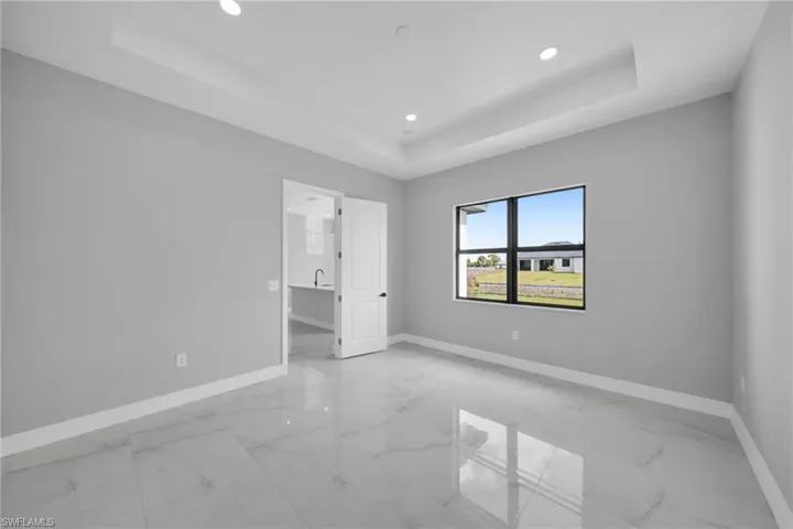 Unfurnished bedroom with a tray ceiling, recessed lighting, and light marble finish floors