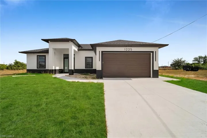 Prairie-style home with a front yard, stucco siding, driveway, and roof with shingles