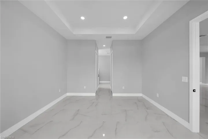 Spare room featuring a tray ceiling, recessed lighting, and light marble finish flooring
