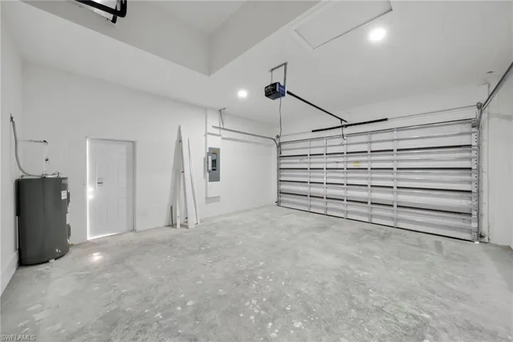 Garage with electric water heater, electric panel, and a garage door opener