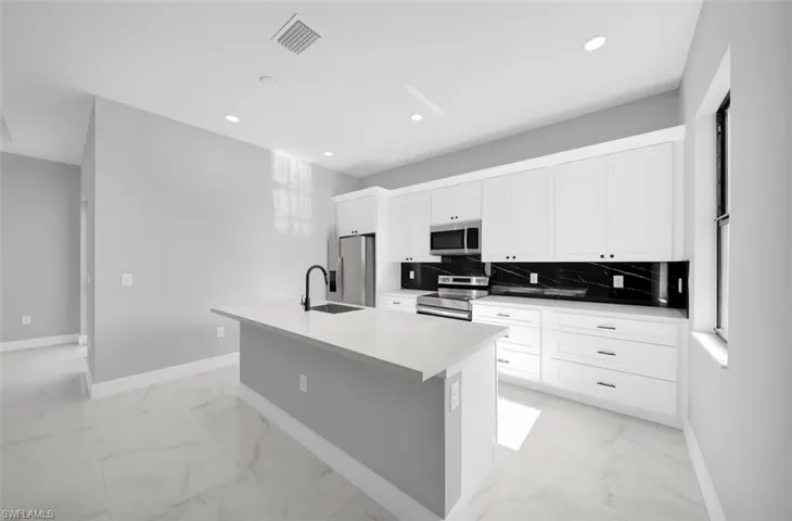 Kitchen with a center island with sink, stainless steel appliances, white cabinetry, light marble finish flooring, and backsplash