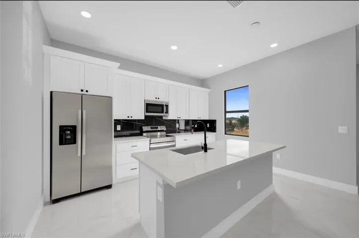Kitchen featuring stainless steel appliances, an island with sink, white cabinetry, light stone counters, and recessed lighting