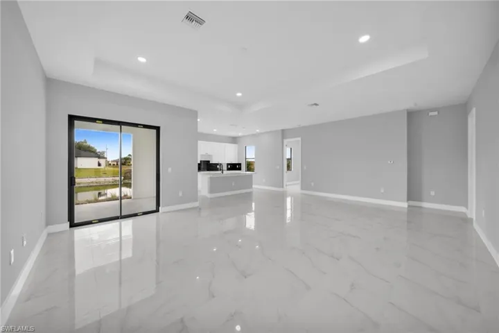 Unfurnished living room featuring a tray ceiling, recessed lighting, and light marble finish floors