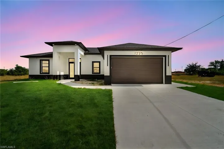 Prairie-style house featuring concrete driveway, a front yard, stucco siding, and an attached garage
