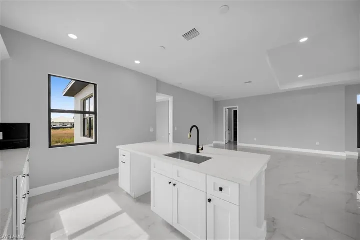 Kitchen with white cabinetry, light marble finish floors, light stone counters, recessed lighting, and an island with sink
