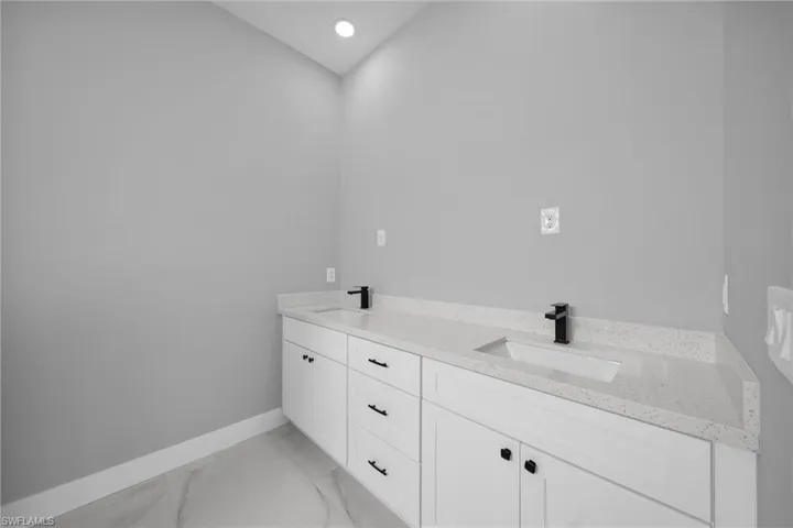 Full bath with double vanity, light marble finish flooring, and recessed lighting