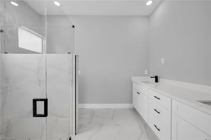Full bathroom with double vanity, light marble finish floors, a marble finish shower, and recessed lighting