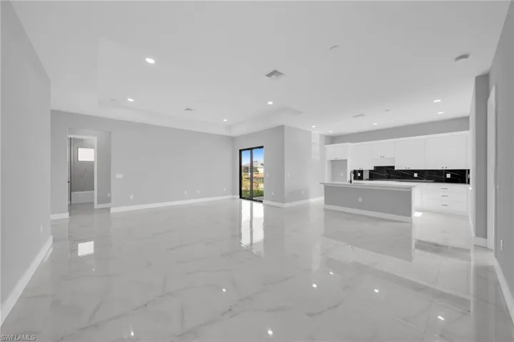 Unfurnished living room with recessed lighting, light marble finish floors, and a raised ceiling