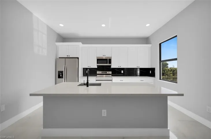 Kitchen with white cabinets, stainless steel appliances, a kitchen island with sink, decorative backsplash, and light stone countertops