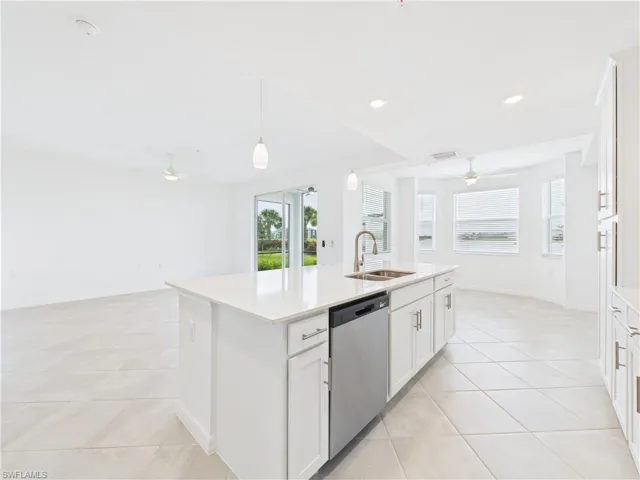 Kitchen with stainless steel dishwasher, a ceiling fan, open floor plan, a kitchen island with sink, and light countertops