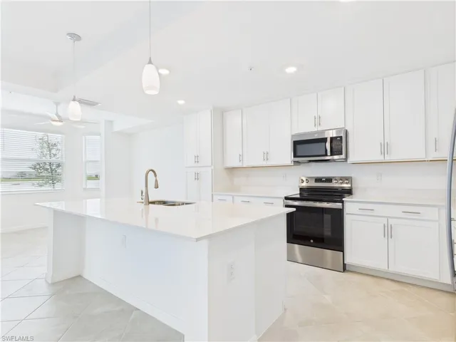 Kitchen featuring appliances with stainless steel finishes, light countertops, white cabinets, light tile patterned floors, and a kitchen island with sink