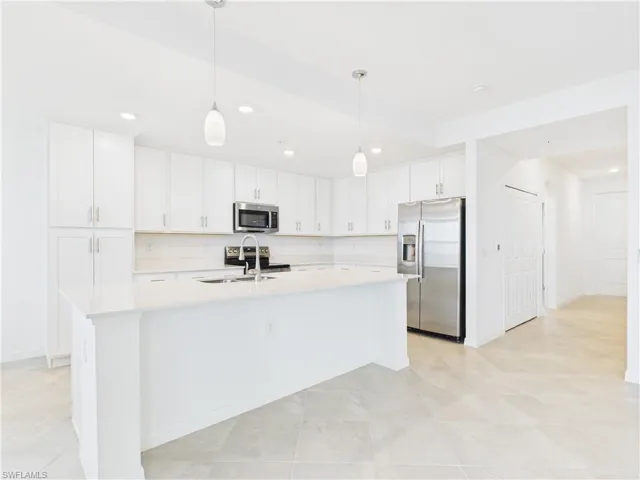 Kitchen with stainless steel appliances, light countertops, white cabinetry, an island with sink, and recessed lighting