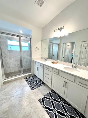 Bathroom with tile floors, dual sinks, a shower with shower door, and large vanity