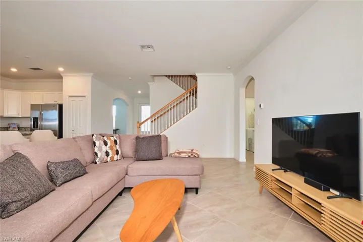 Living area with ornamental molding, arched walkways, recessed lighting, light tile patterned floors, and stairway