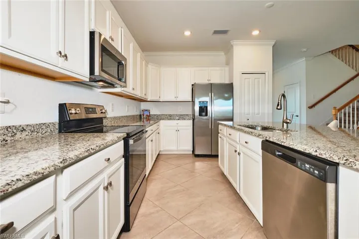 Kitchen featuring appliances with stainless steel finishes, light stone counters, crown molding, white cabinets, and light tile patterned floors