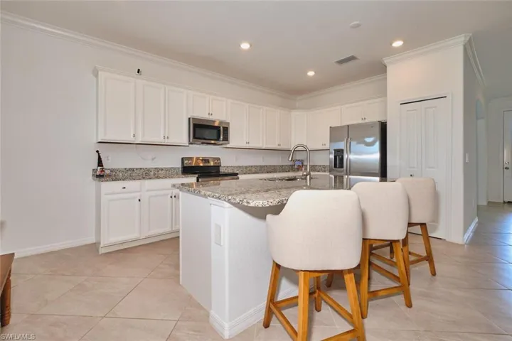 Kitchen with white cabinetry, light stone counters, a breakfast bar area, crown molding, and stainless steel appliances