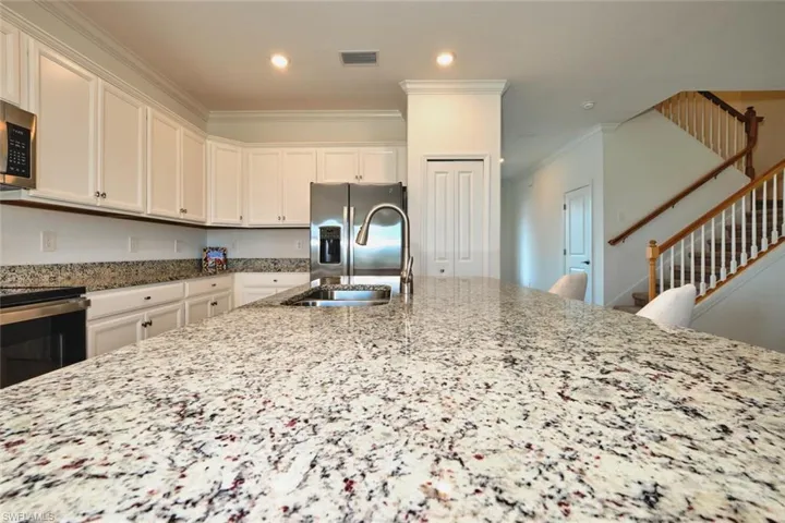 Kitchen featuring light stone countertops, ornamental molding, stainless steel appliances, white cabinetry, and recessed lighting